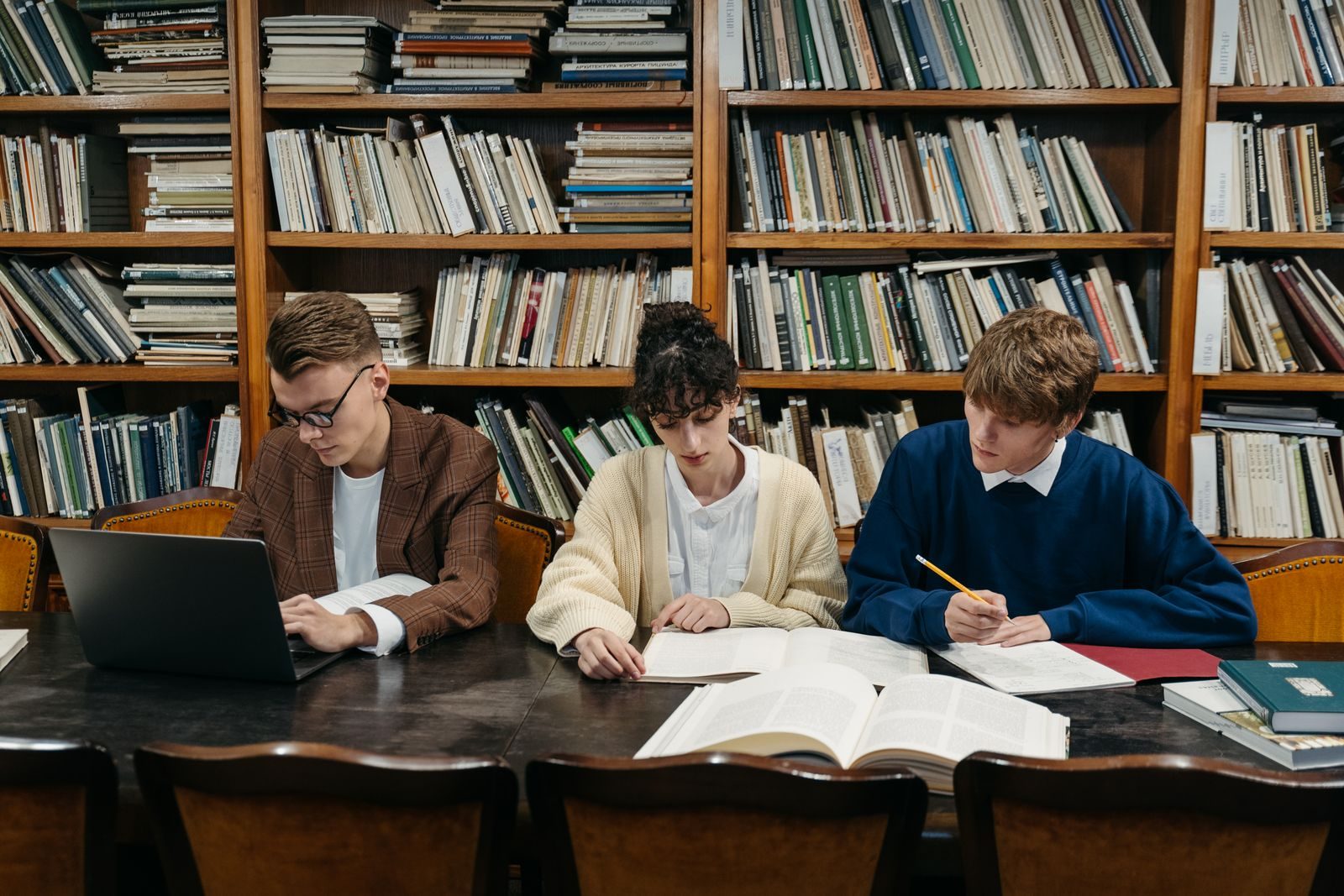 Three students studying with books and a laptop at a library table