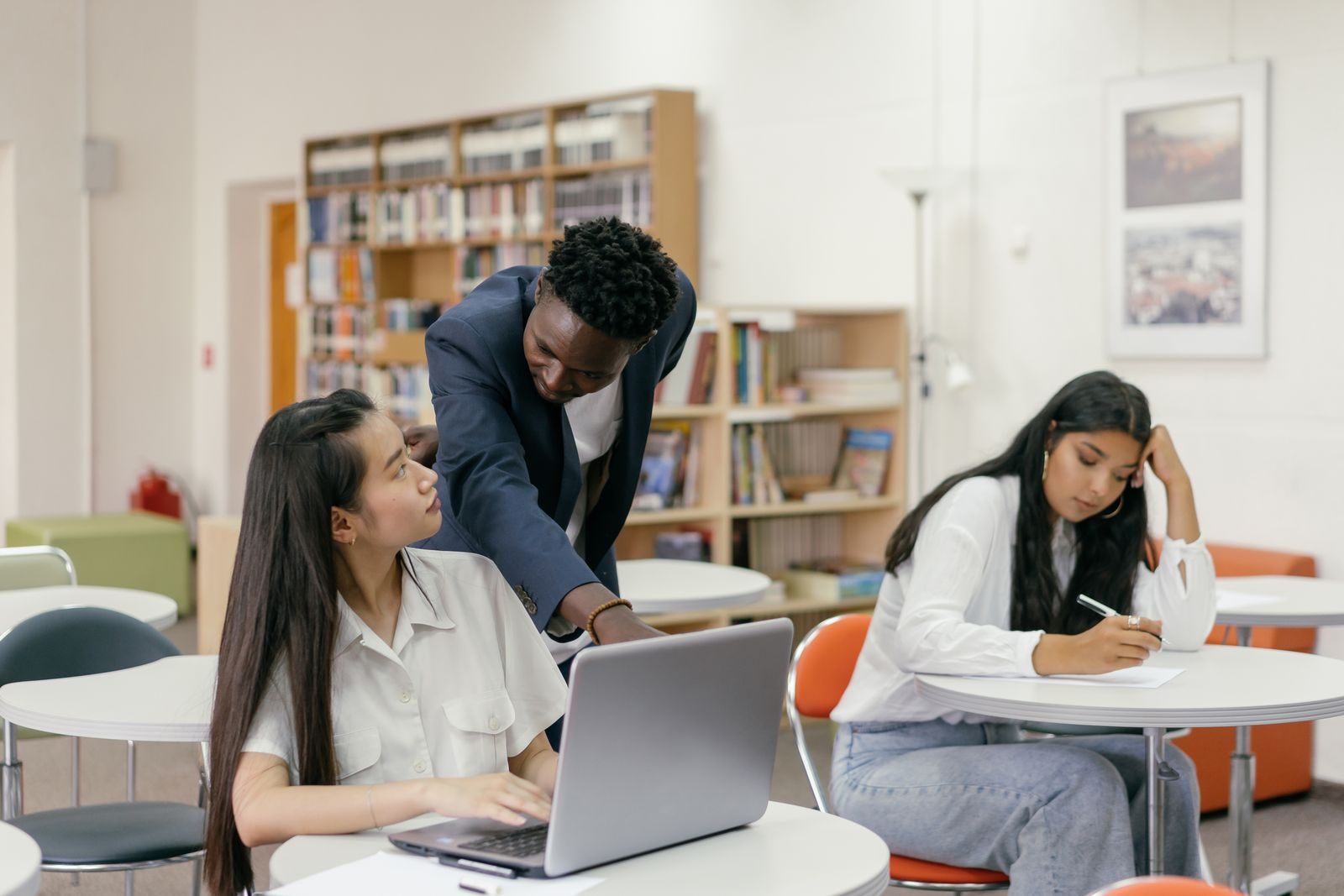 A tutor leaning over to point at a student’s laptop in a bright classroom