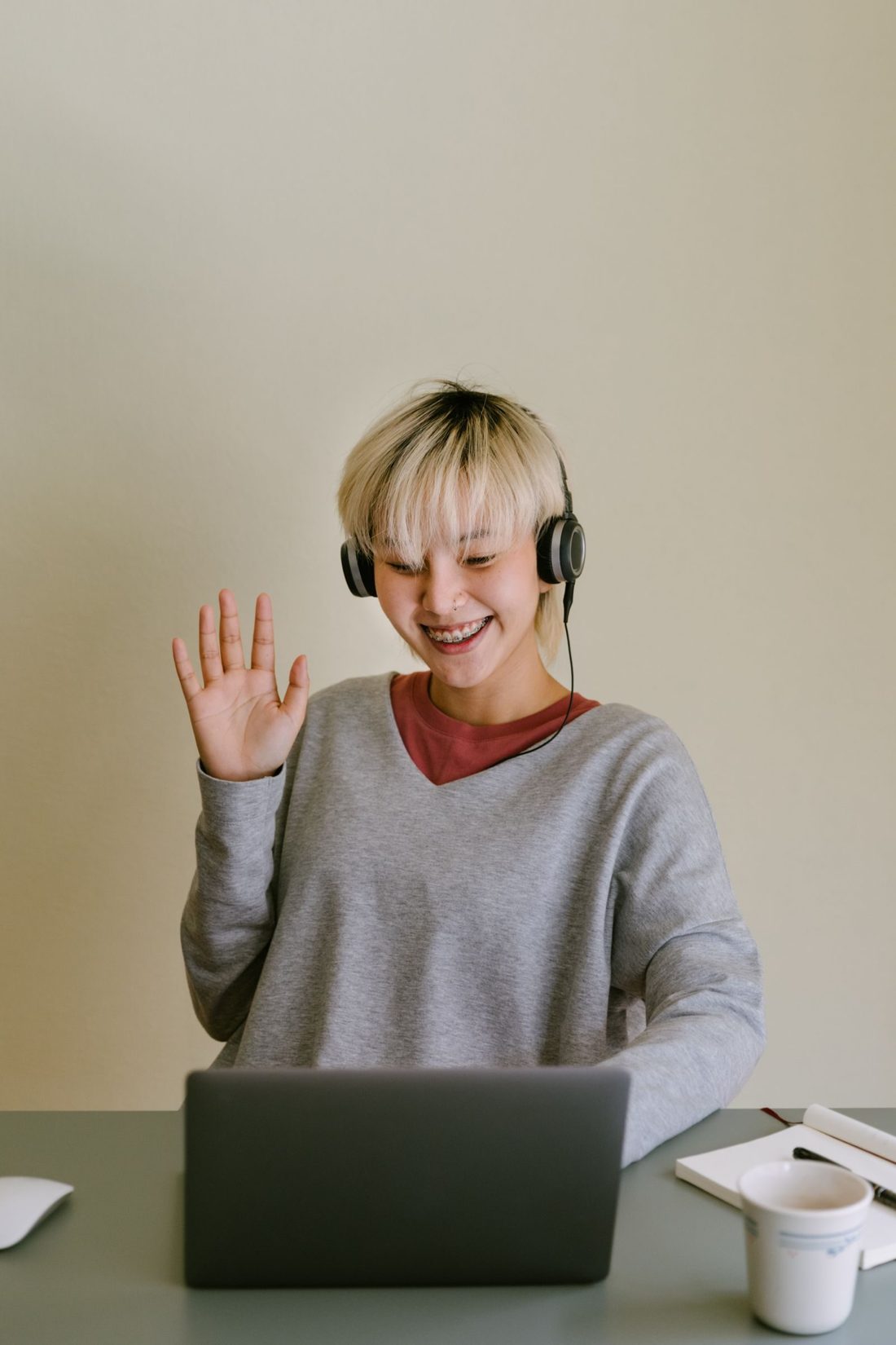 A smiling student in headphones waving to a tutor on a video call