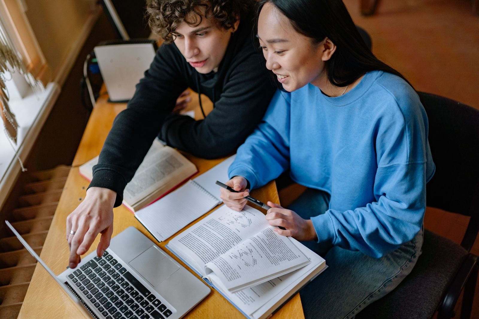 Two students working through a textbook together at a laptop