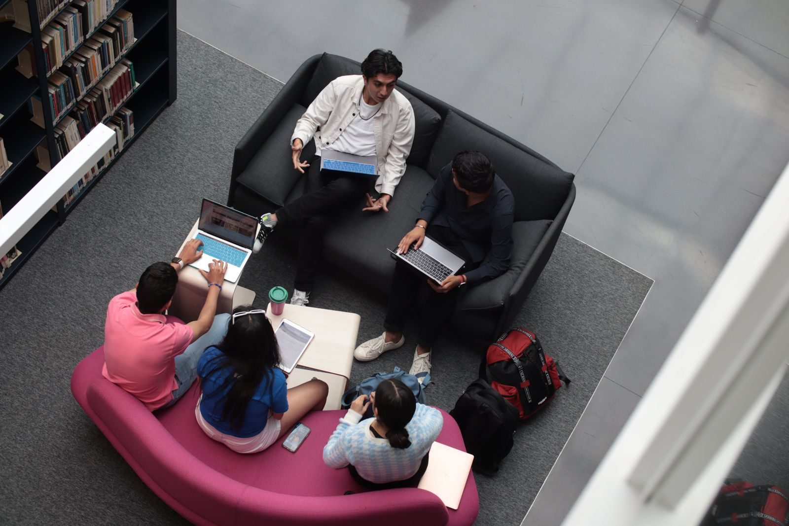 A small study group with laptops on sofas in a library, seen from above