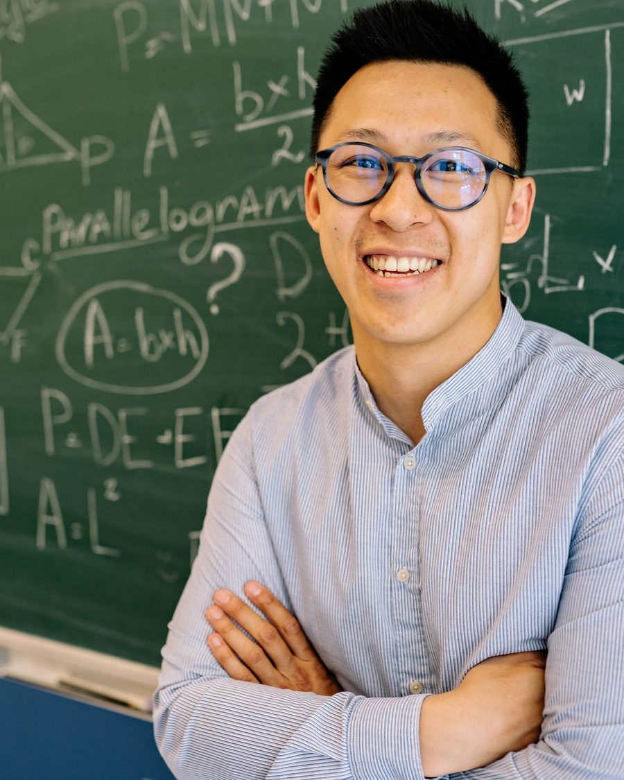Portrait of a smiling man in glasses in front of a chalkboard of equations